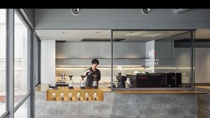 Interior de una cafetería moderna con un barista preparando bebidas, una máquina de café y una exhibición de granos de café.
