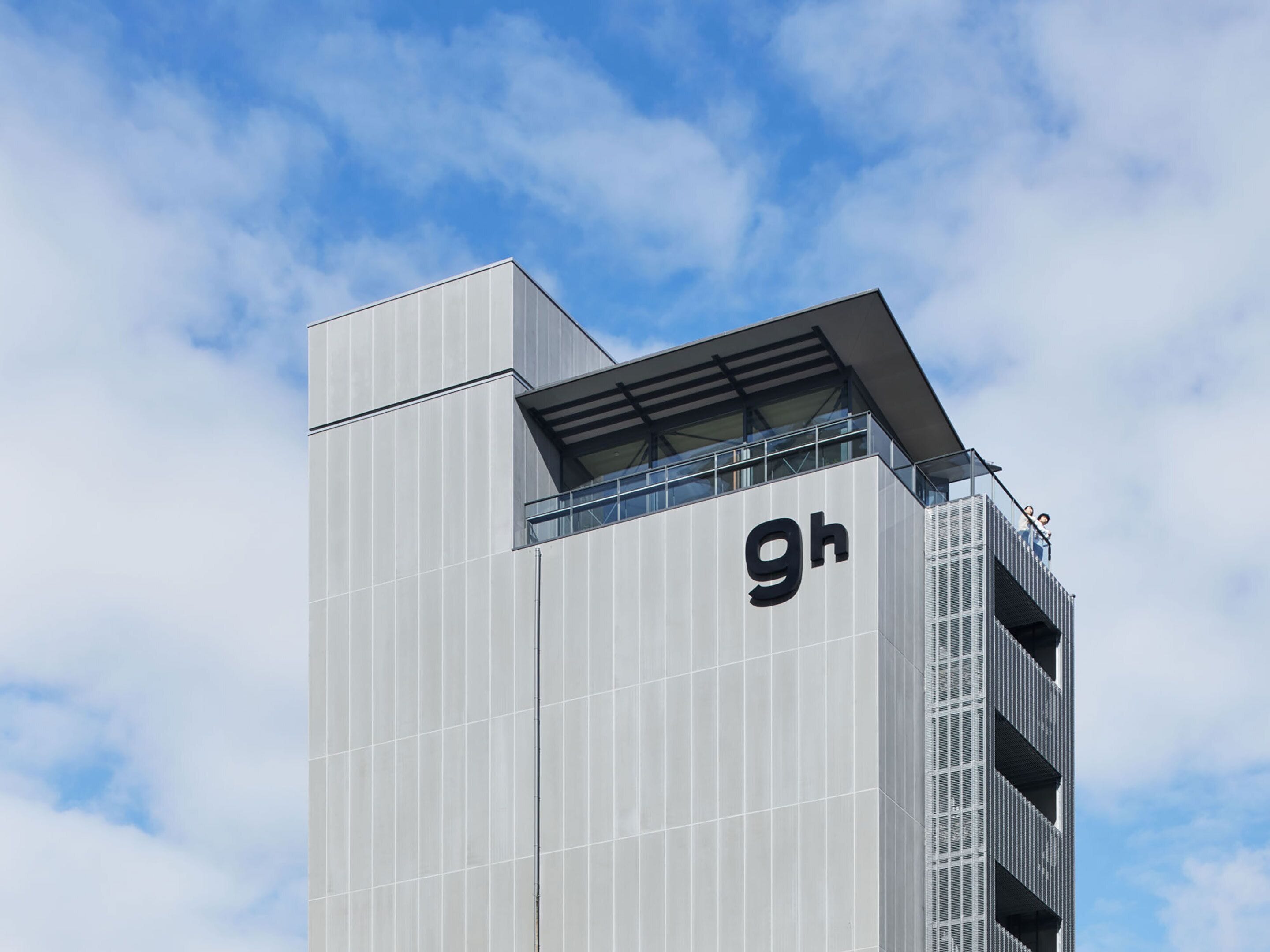 En moderne bygning med et tydeligt 'gh'-logo, der har et unikt arkitektonisk design med et skråt tag og en balkon.