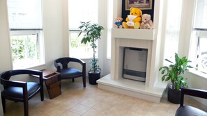 A living room with a fireplace, two chairs, a small table, and two potted plants.