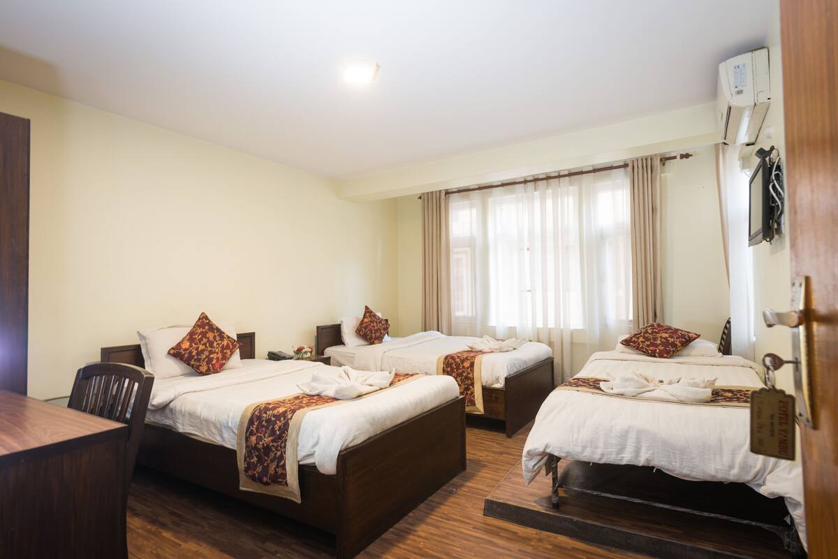 A hotel room with two beds, wooden flooring, a desk, and a window with curtains.
