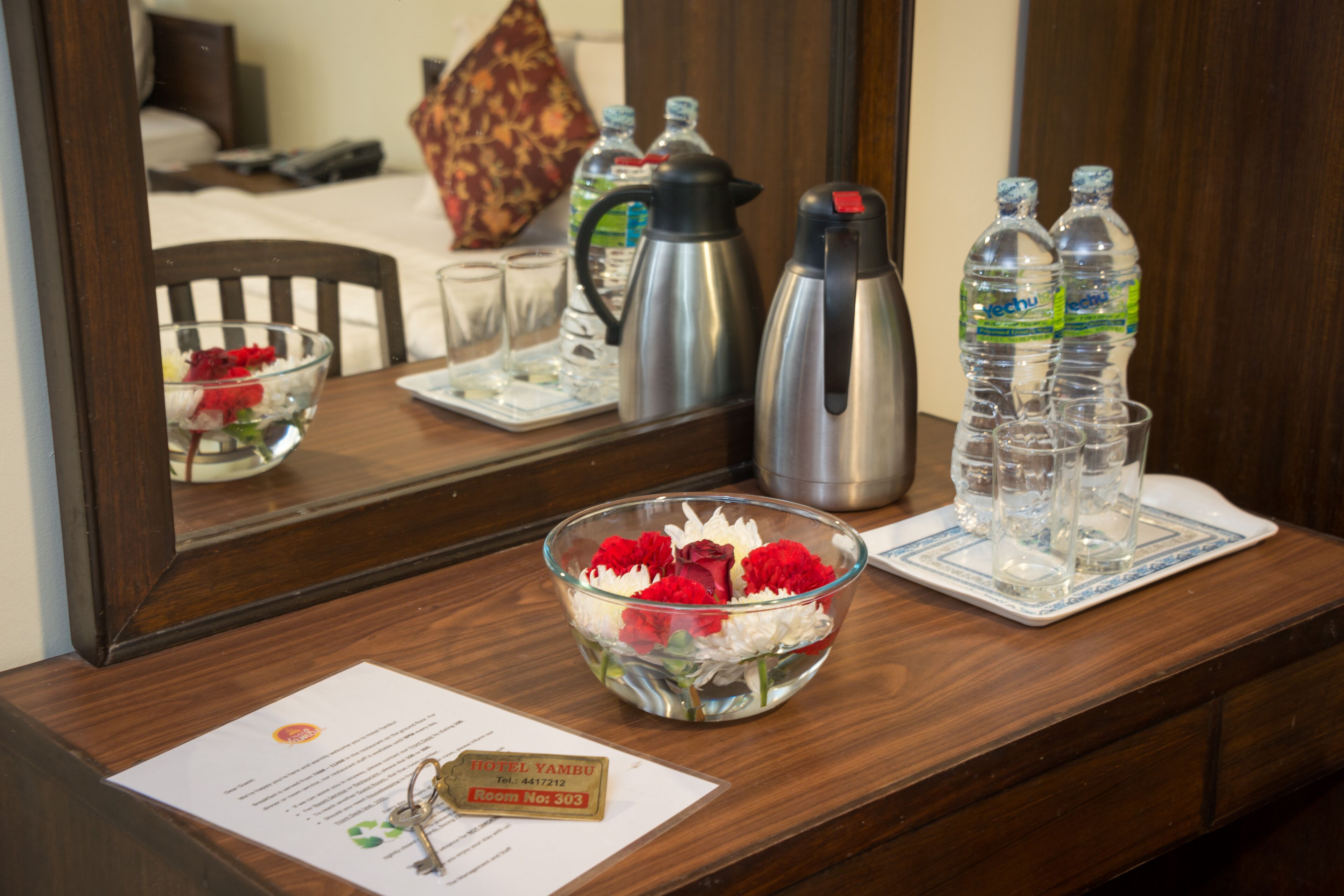 A hotel reception desk with a glass bowl of flowers, a coffee pot, water bottles, and a key card holder.