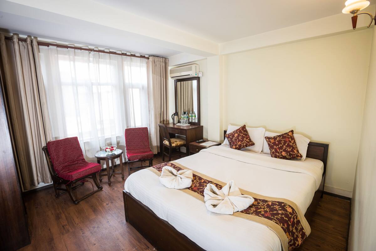 A hotel room with a large bed, a desk, a chair, a small table, and a mirror.