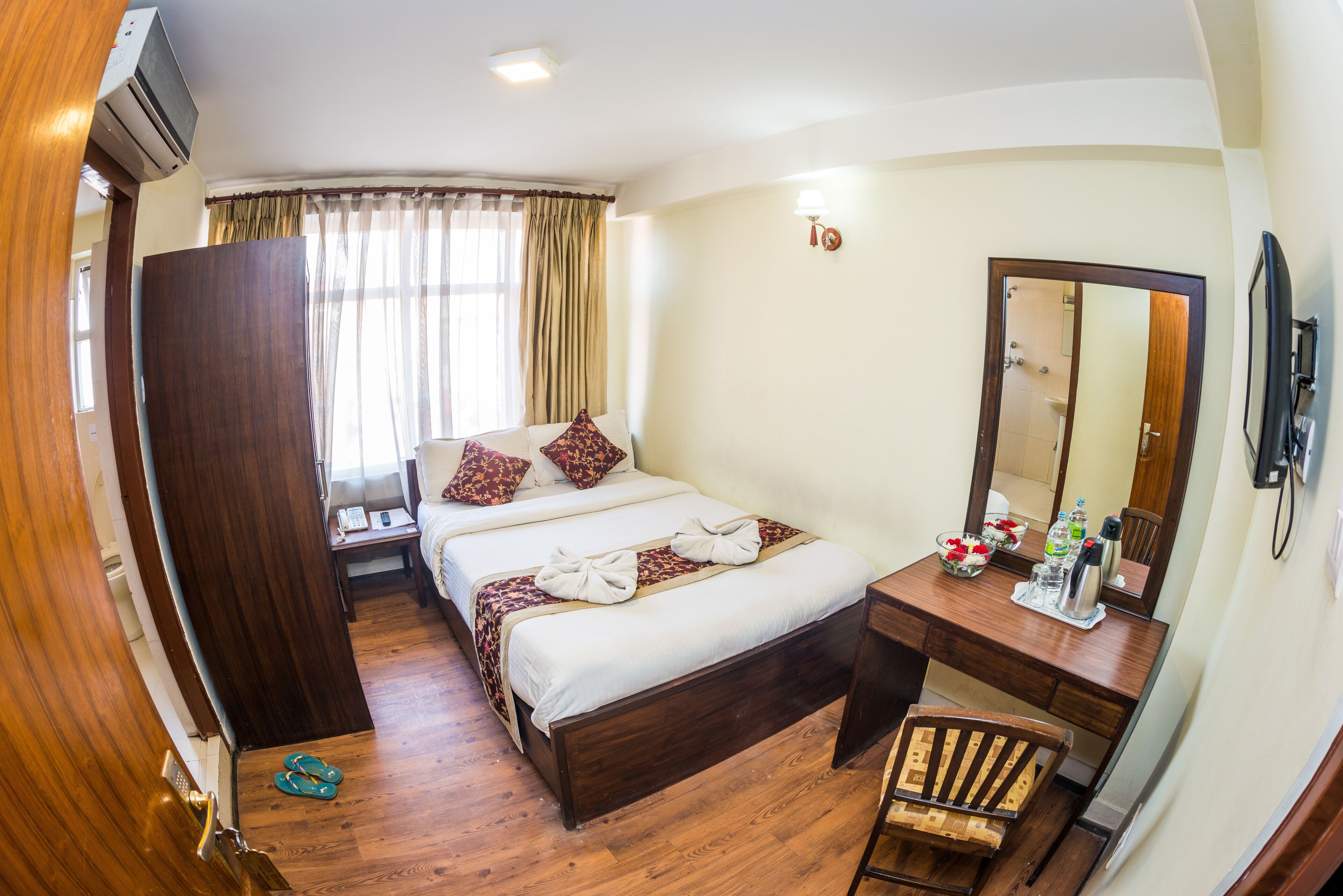 A hotel room with a wooden bed, a desk with a mirror, and a small chair.