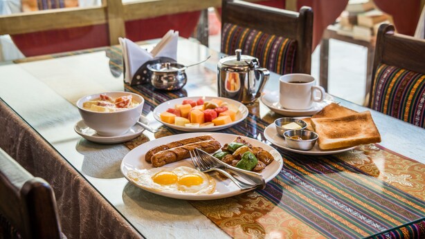 A breakfast table with plates of eggs, sausages, toast, and fruit. - Hotel Yambu (Kathmandu)
