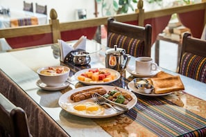 A breakfast table with plates of eggs, sausages, toast, and fruit. - Hotel Yambu (Kathmandu)