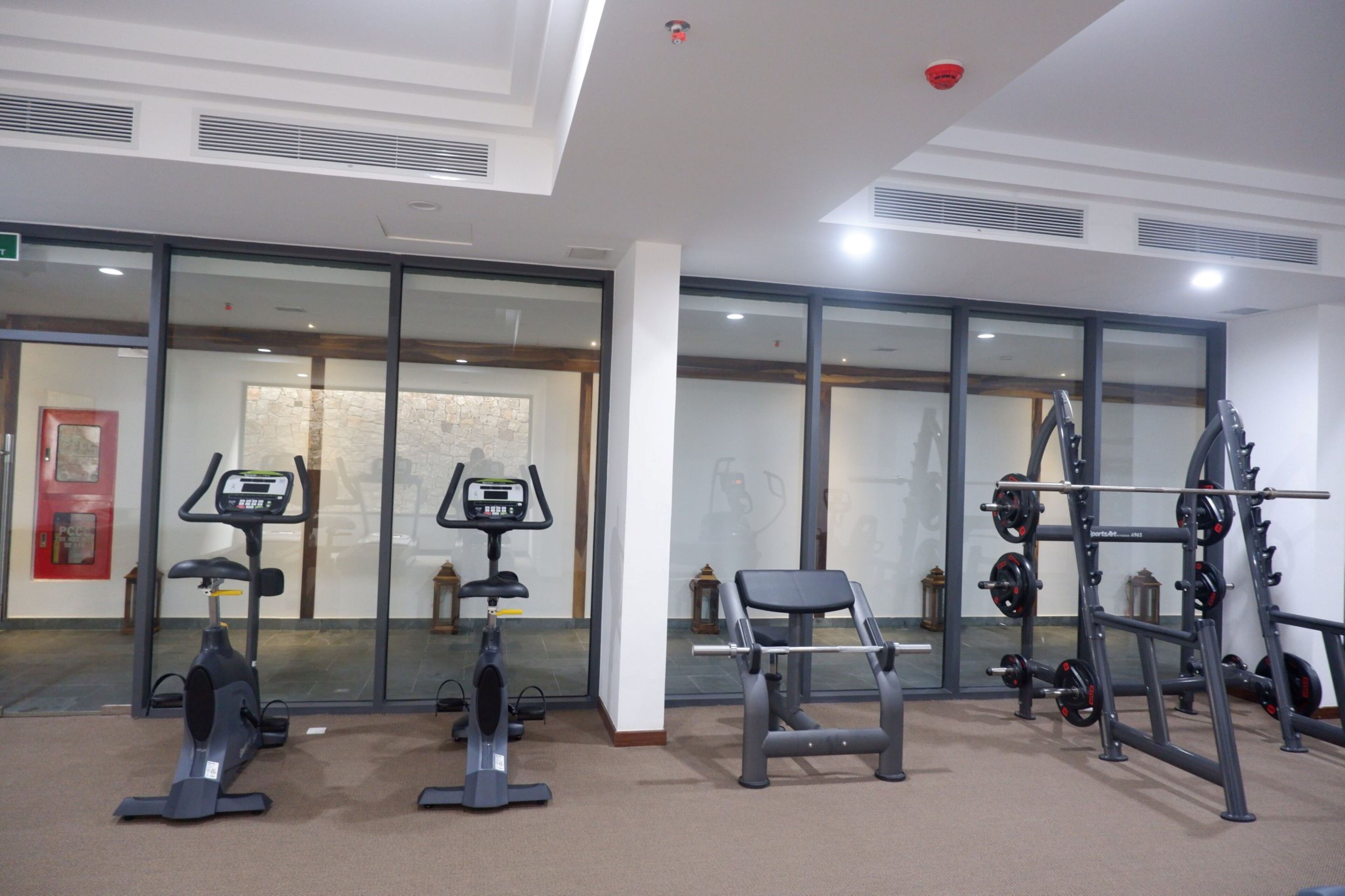 Een fitnessruimte met cardioapparatuur, gewichten en een bank.