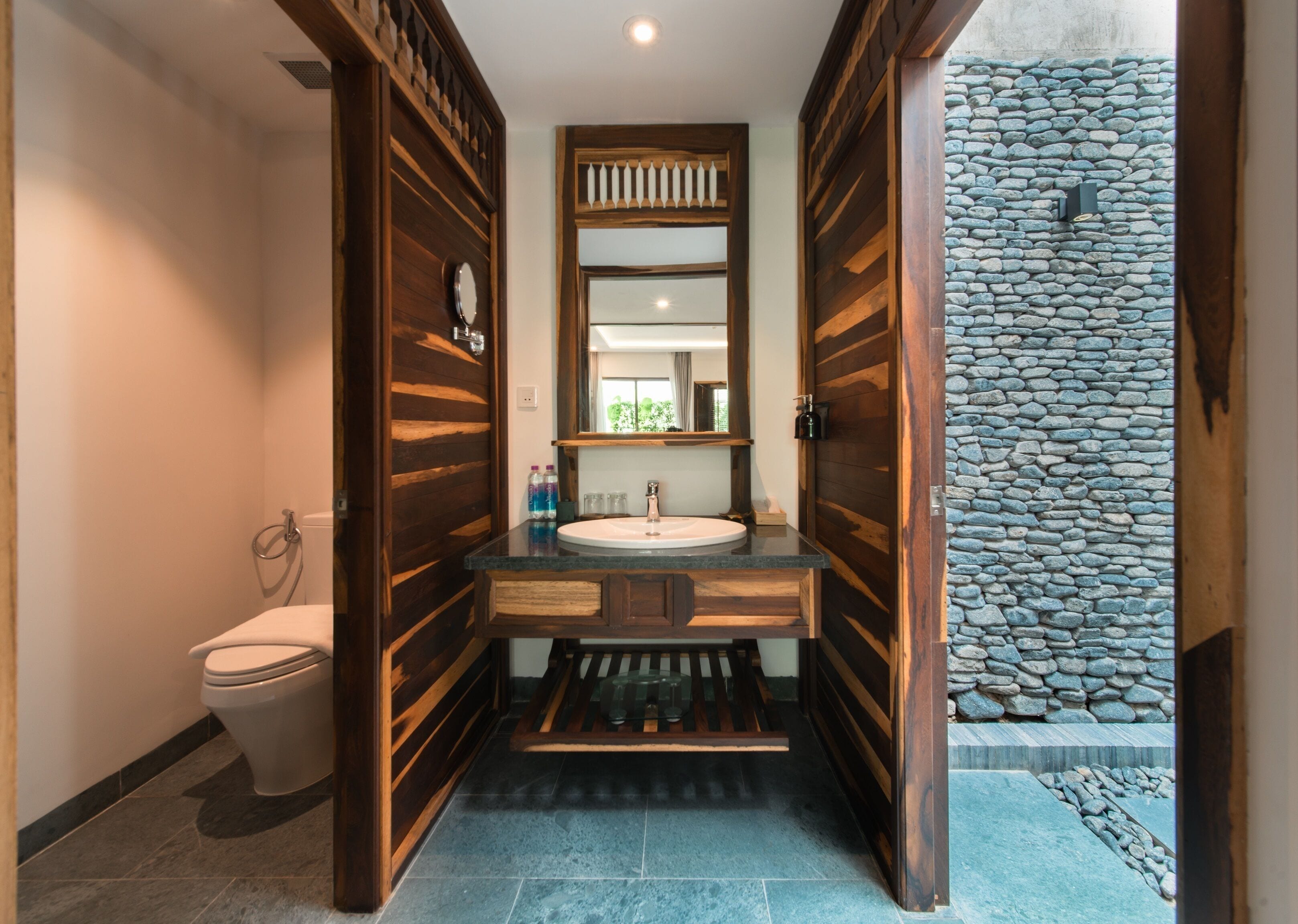 A bathroom with a wooden vanity, a round sink, and a stone wall.