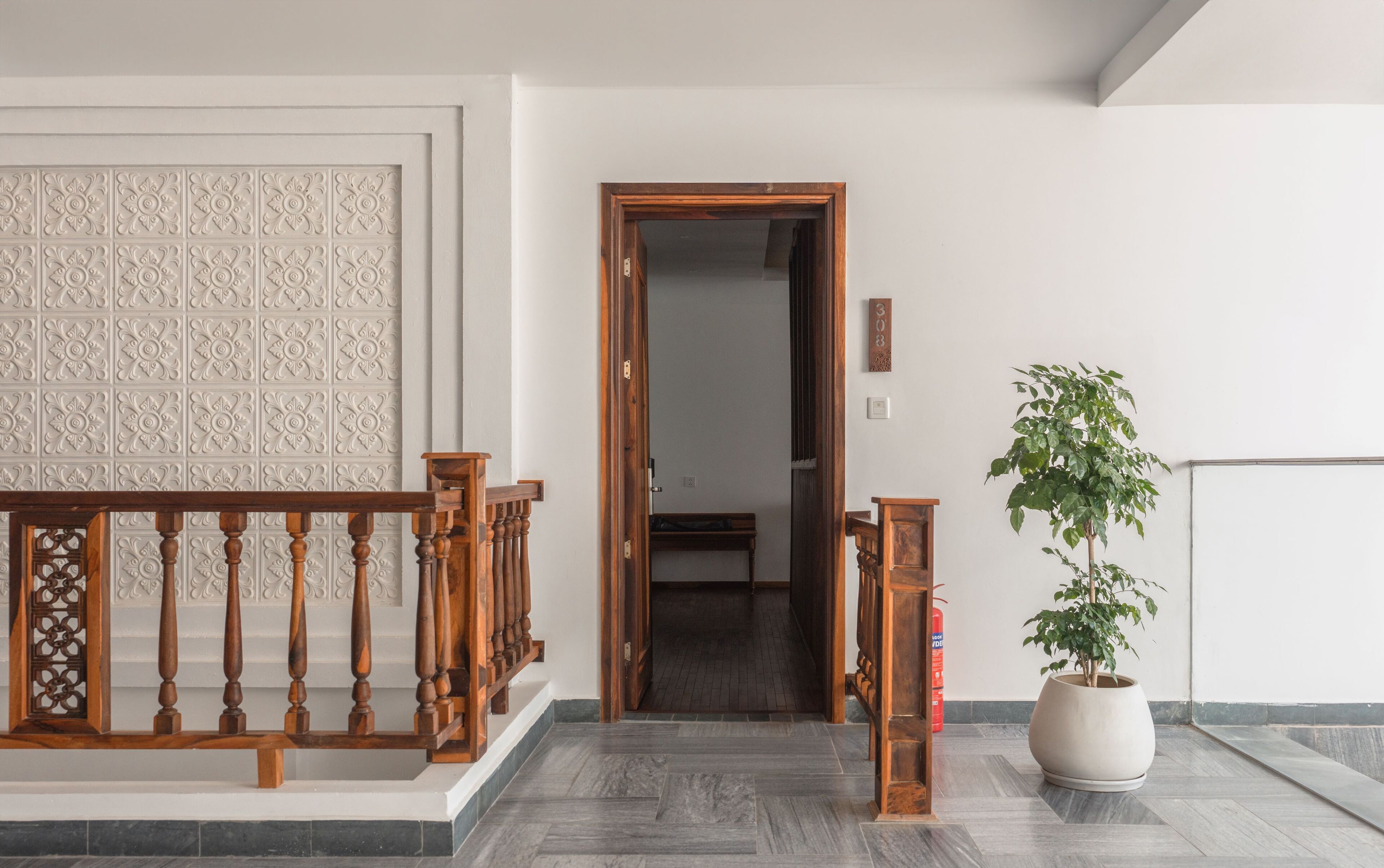 A hallway with a wooden railing, a potted plant, and a door leading to another room.