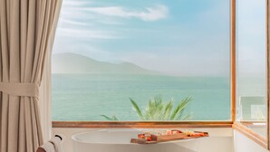 A bathroom with a bathtub, a window with a view of the sea, and a towel rack. - Alibu Resort Nha Trang (Bac Nha Trang)