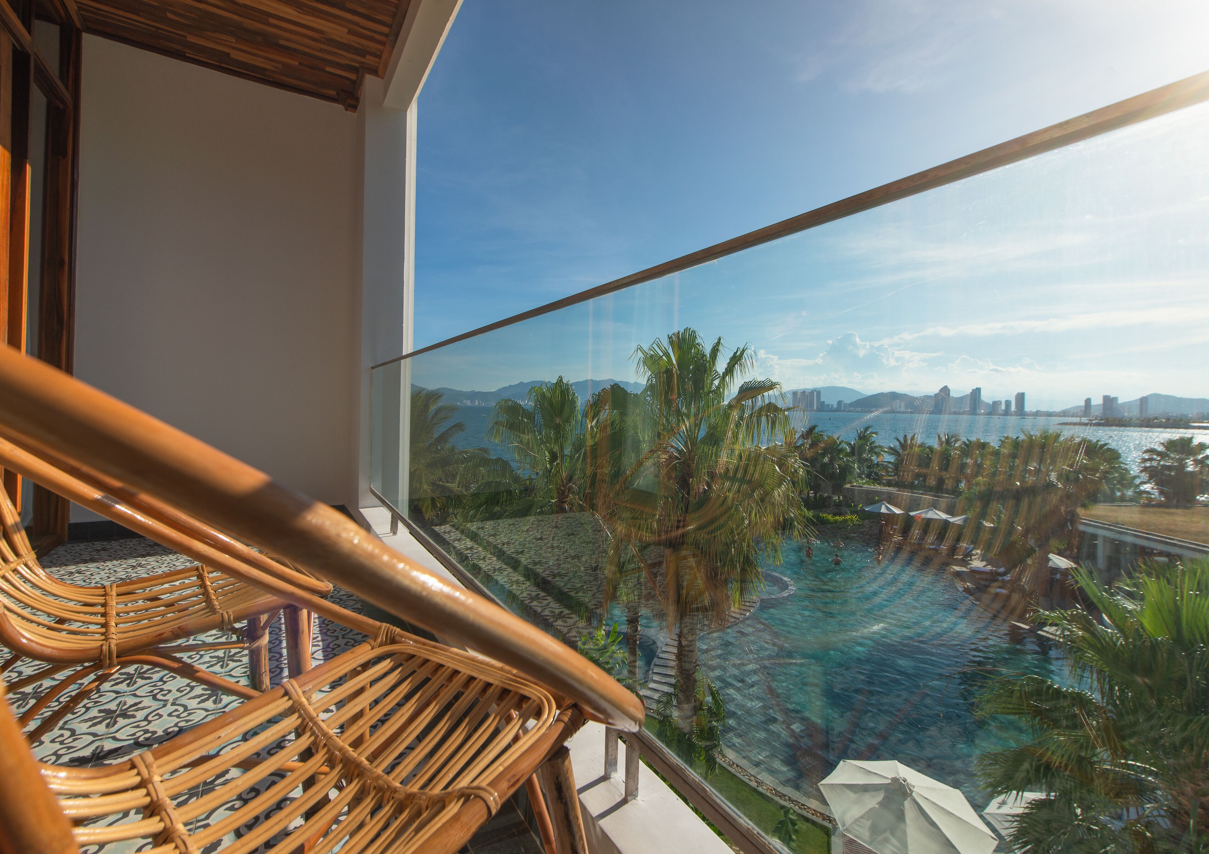 A balcony with wicker chairs overlooking a pool and a cityscape.