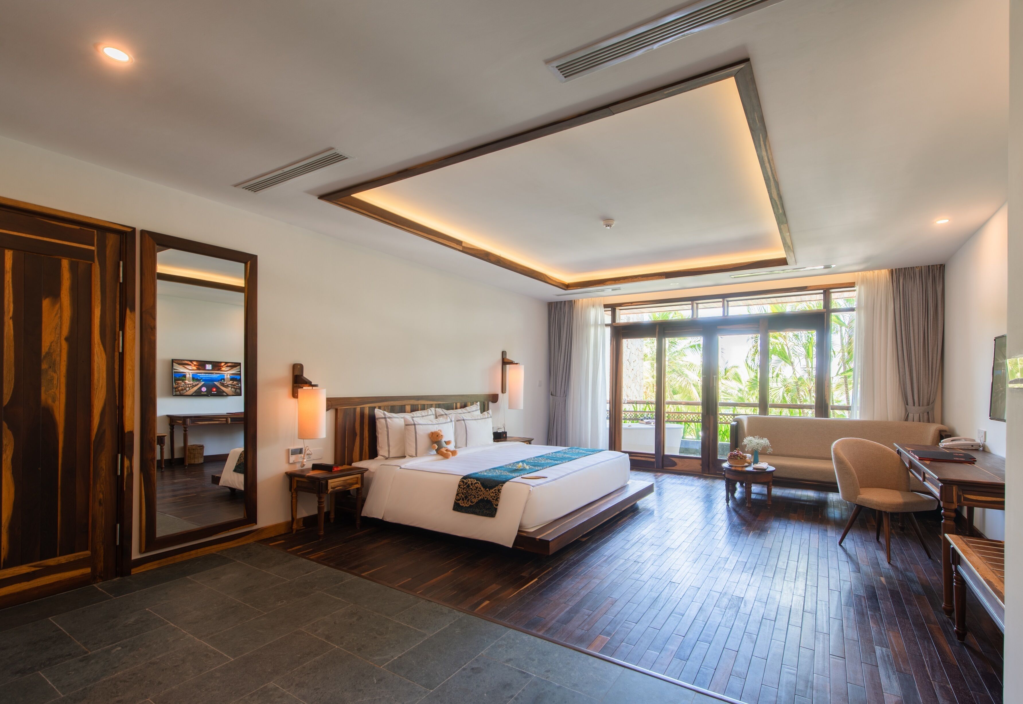 A modern hotel room with a large bed, a sofa, a desk, and a dining table.