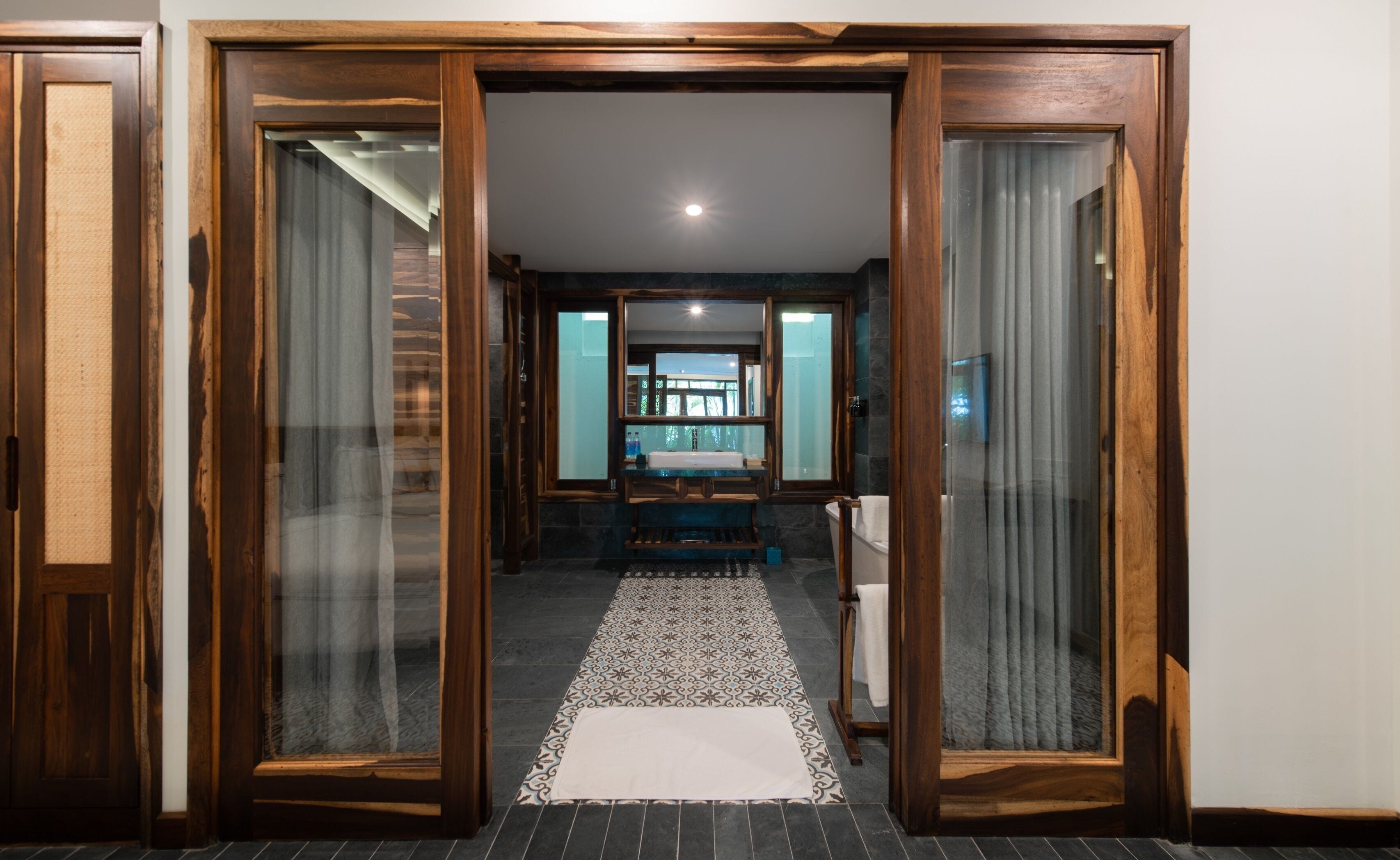 Een gang die leidt naar een badkamer met een wastafel en een spiegel.