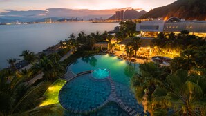 Un resort con una amplia piscina infinita, palmeras y vista al océano al atardecer.