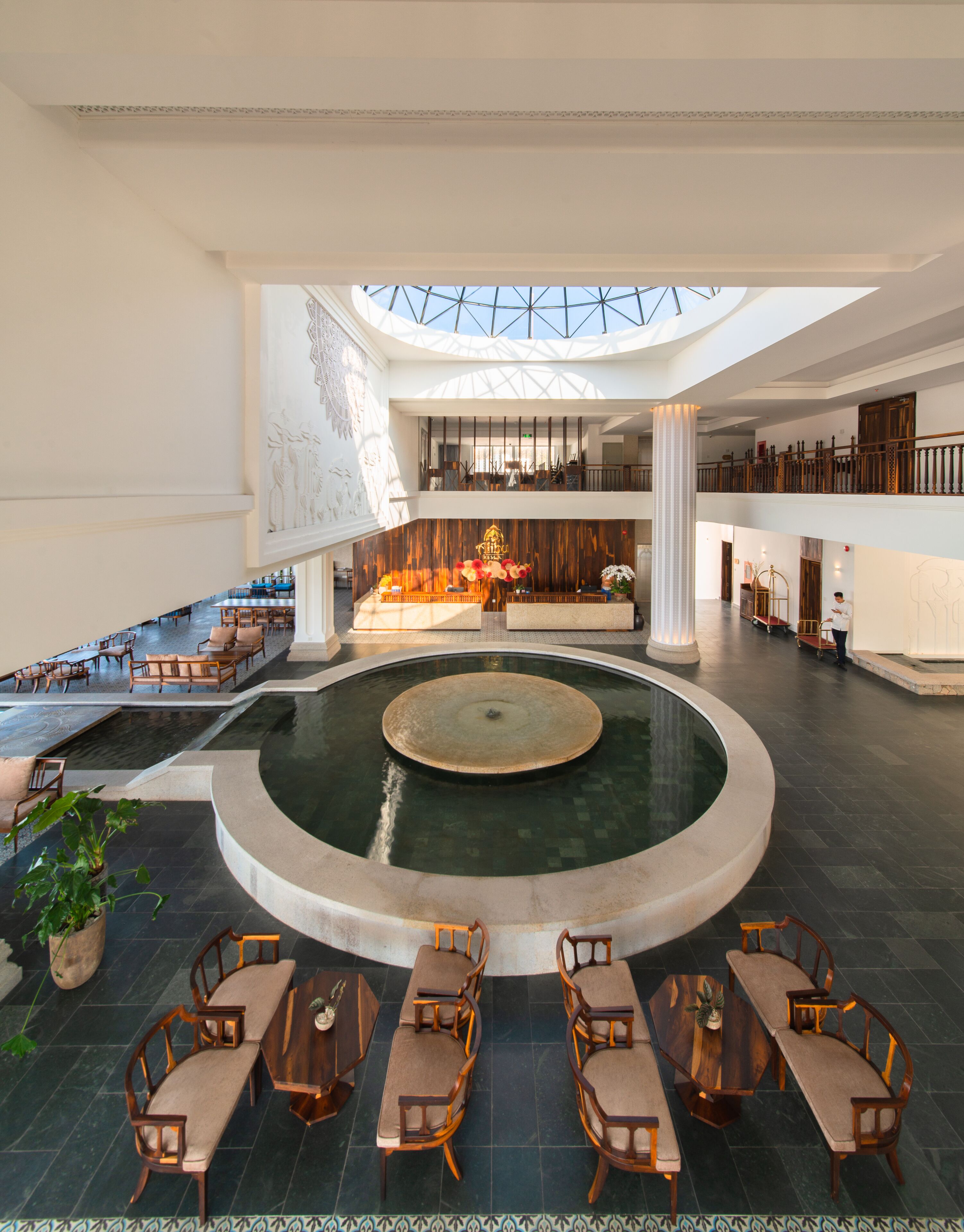 A spacious lobby with a central fountain, multiple seating areas, and a high ceiling with skylights.