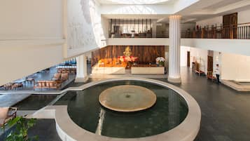 A spacious lobby with a central fountain, multiple seating areas, and a high ceiling with skylights.