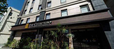 Entrada de hotel con fachada moderna, un cartel que dice "The Cellecton" y una zona ajardinada con diversas plantas.