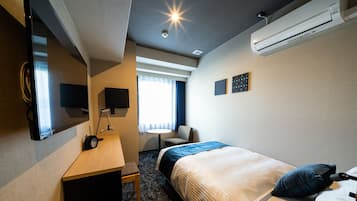 Quarto de hotel com cama, escrivaninha, cadeira, televisão e ar condicionado.