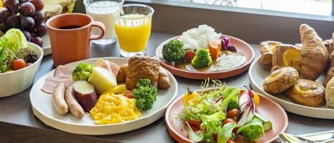 A breakfast table with plates of food, including eggs, sausages, and croissants, and a glass of orange juice.