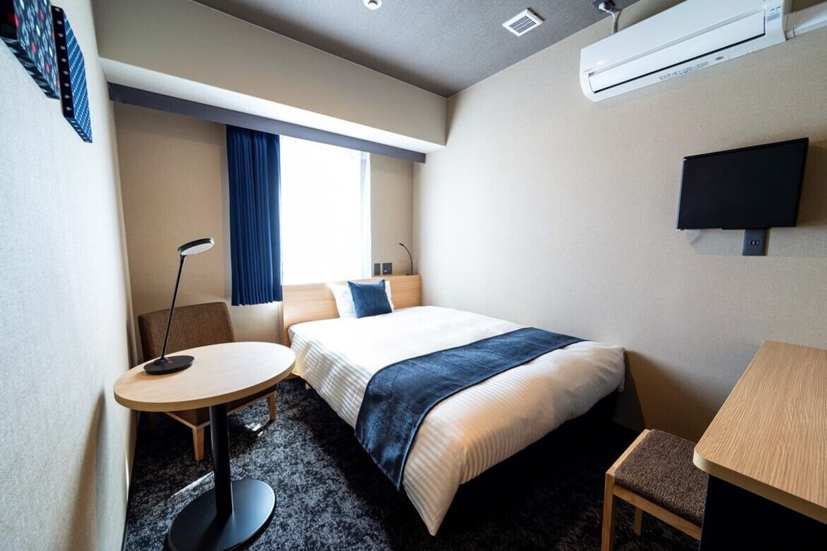 Ein Hotelzimmer mit einem Bett, einem Schreibtisch, einem Stuhl, einem runden Tisch, einem Fernseher und einer Klimaanlage.