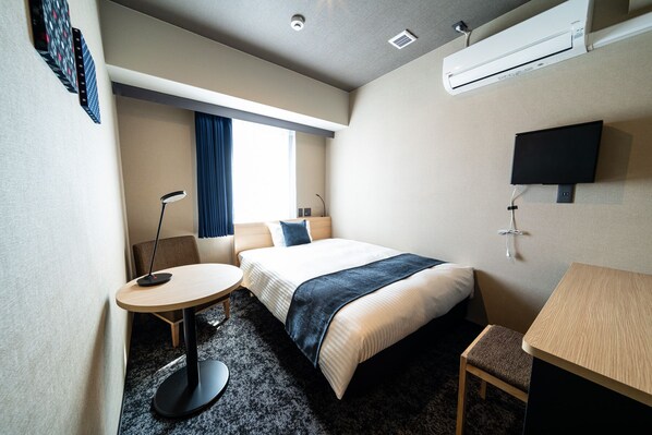 A hotel room with a bed, a desk, a chair, a desk lamp, a TV, and an air conditioning unit. - The Celecton Kurume (Kurume)