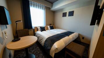 Habitación de hotel con cama, escritorio, silla, mesita y ventana con cortinas.