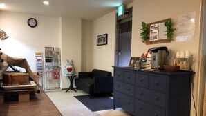 A cozy hotel room with a wooden table, a dark blue dresser, a small round table with a decorative item, a clock on the wall, and a bulletin board with various notices. - Hotel Arima Koukaen (Nishinomiya)