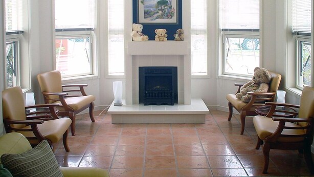 A living room with a fireplace, two armchairs, a sofa, and a window with blinds.
