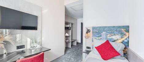 Una habitación de hotel moderna con una televisión de pantalla plana, un escritorio, una cama con ropa de cama roja y blanca, y una pintura de un paisaje urbano en la pared.
