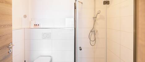 Un baño moderno con ducha envuelta en vidrio, inodoro y lavamanos con dispensador de jabón.