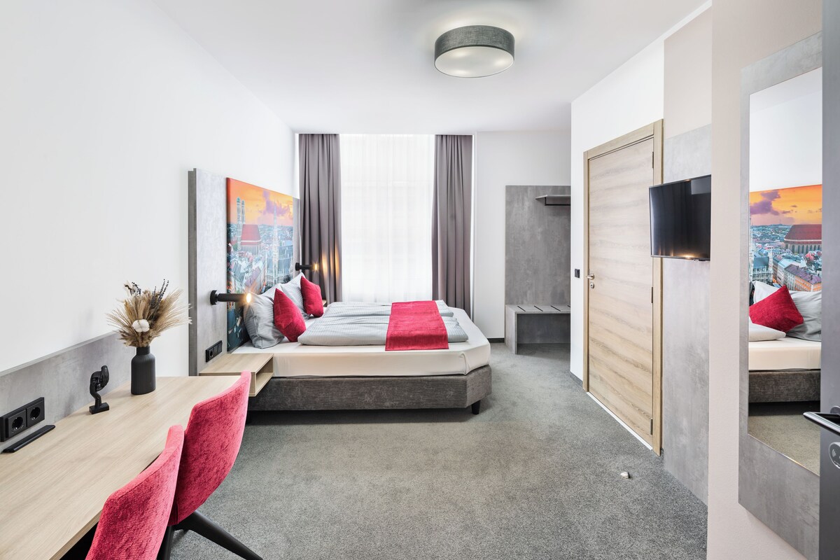 Una habitación de hotel moderna con cama, escritorio, silla, televisión y obras de arte en las paredes.