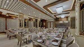 Un amplio comedor con varias mesas dispuestas para comer, con una moderna lámpara de araña y paneles decorativos en el techo.