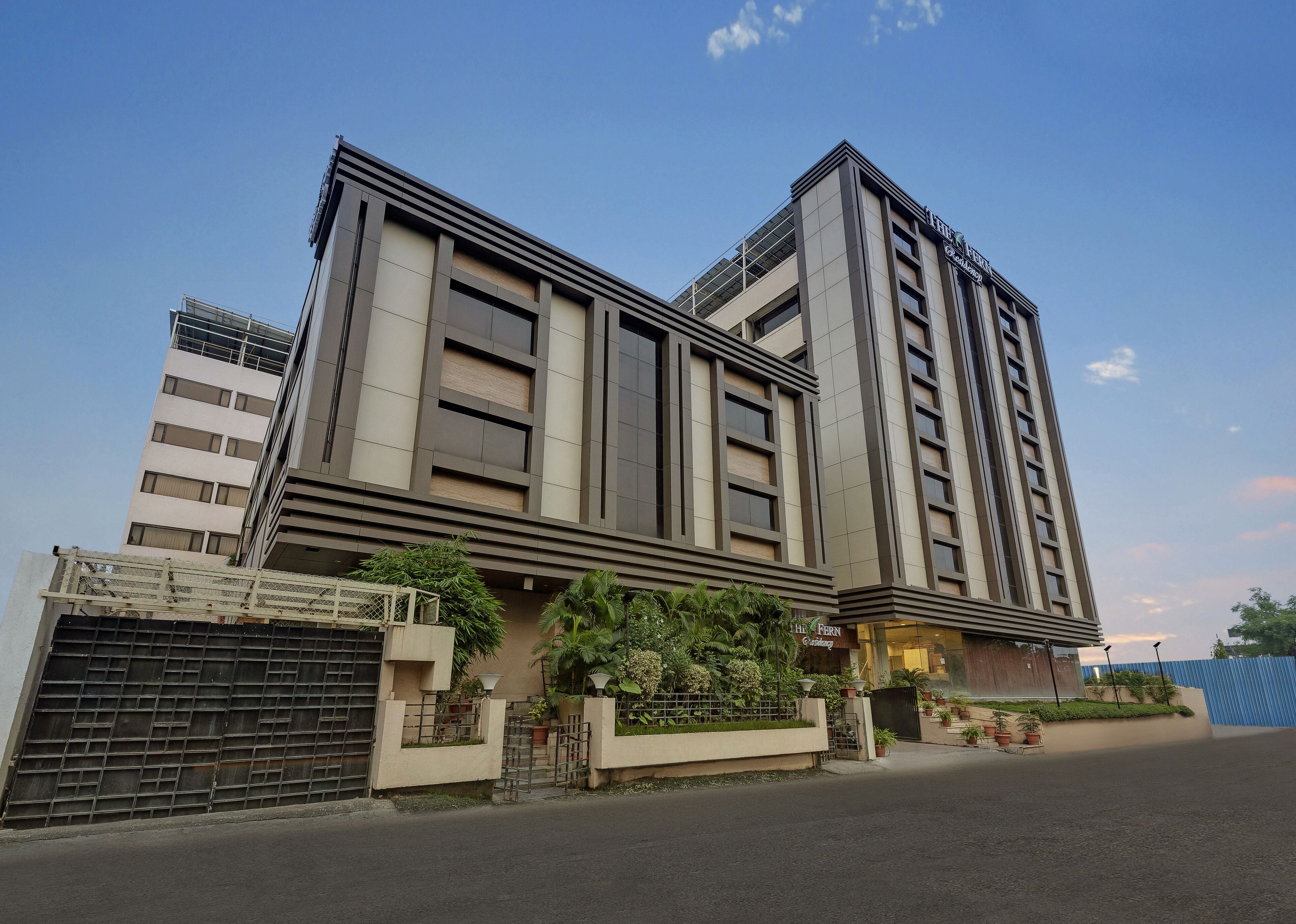 A modern multi-story building with a prominent entrance, large windows, and a gated driveway.