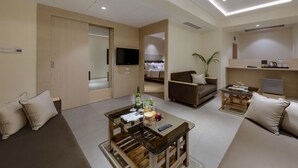Una habitación de hotel moderna con sofá, una mesa de centro de vidrio, televisión, cama y una zona de kitchenette.