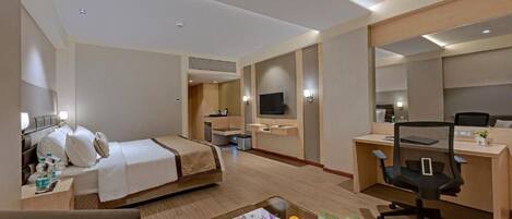 A hotel room with a bed, desk, chair, and a small table with a plant and fruit.