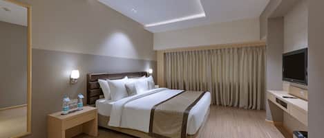 A modern hotel room with a large bed, bedside table with water bottles, a TV, and a desk.