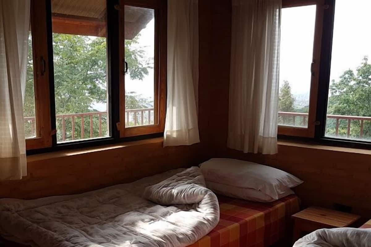 Ein Einzelbett mit kariertem Bettbezug und weißen Kissen, ein Nachttisch aus Holz und ein Fenster mit Vorhängen.