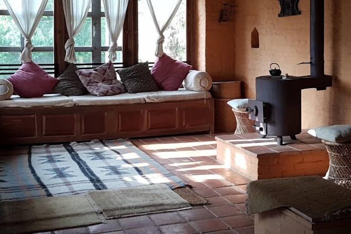Ein gemütliches Zimmer mit integrierter Sitzbank, Kaminofen und Blick durch große Fenster.