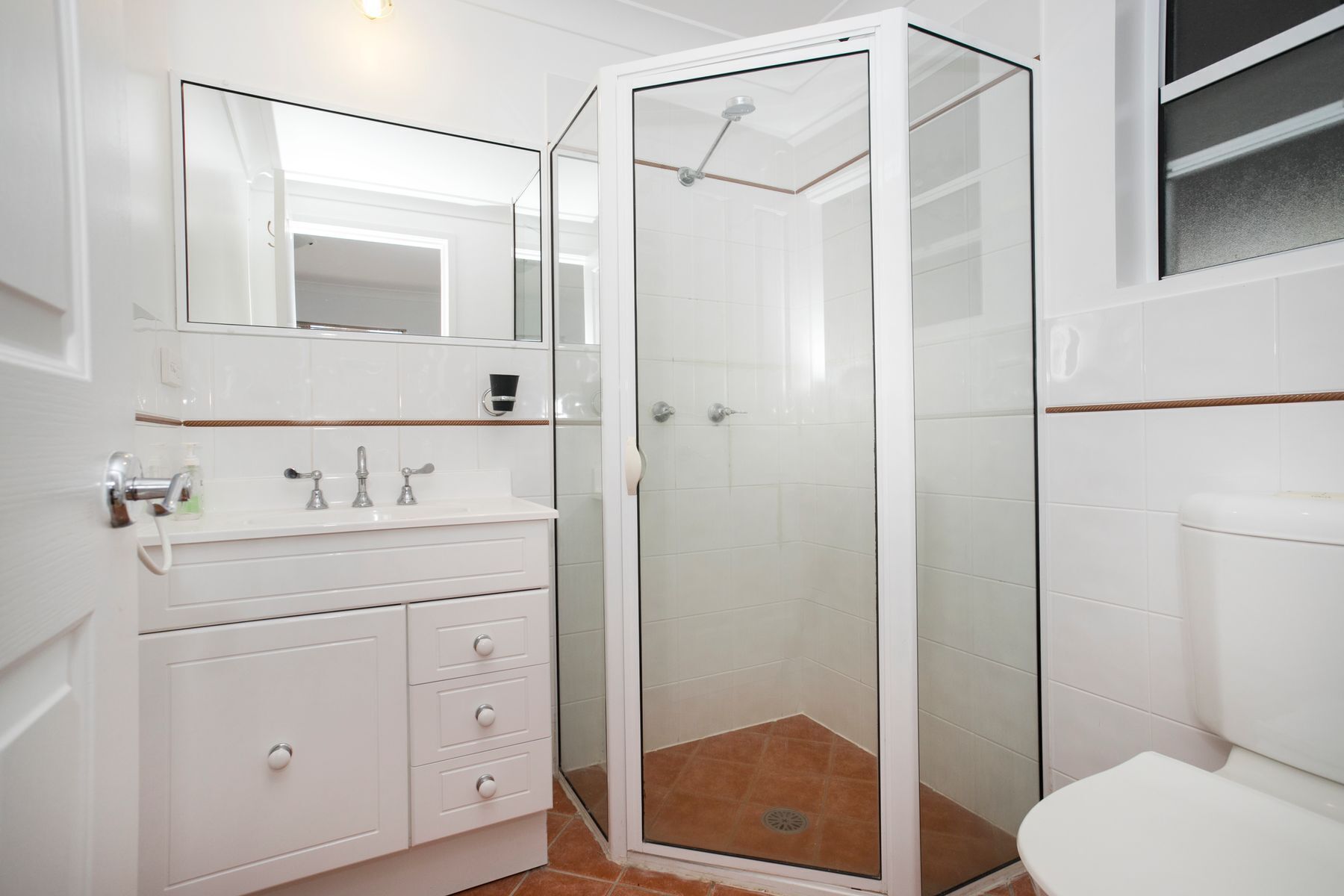Un bagno moderno con doccia in vetro, sanitari bianchi e un ampio specchio sopra il lavabo.