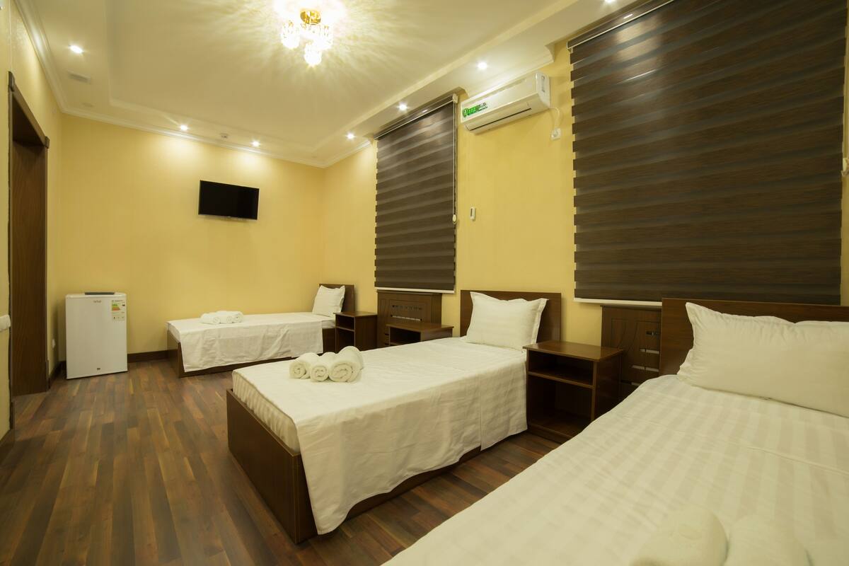 A hotel room with two beds, a TV, an air conditioner, and a small refrigerator.
