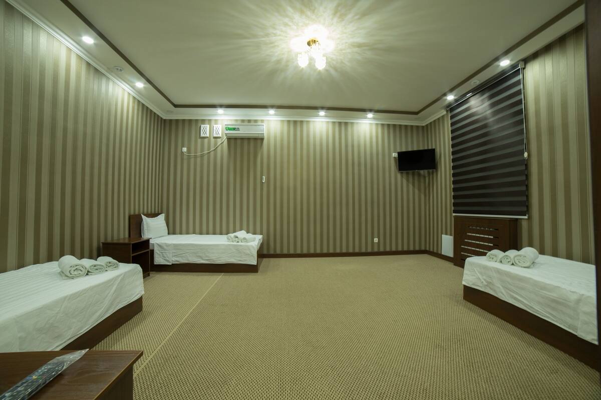 A hotel room with two beds, a flat-screen TV, an air conditioning unit, and a carpeted floor.