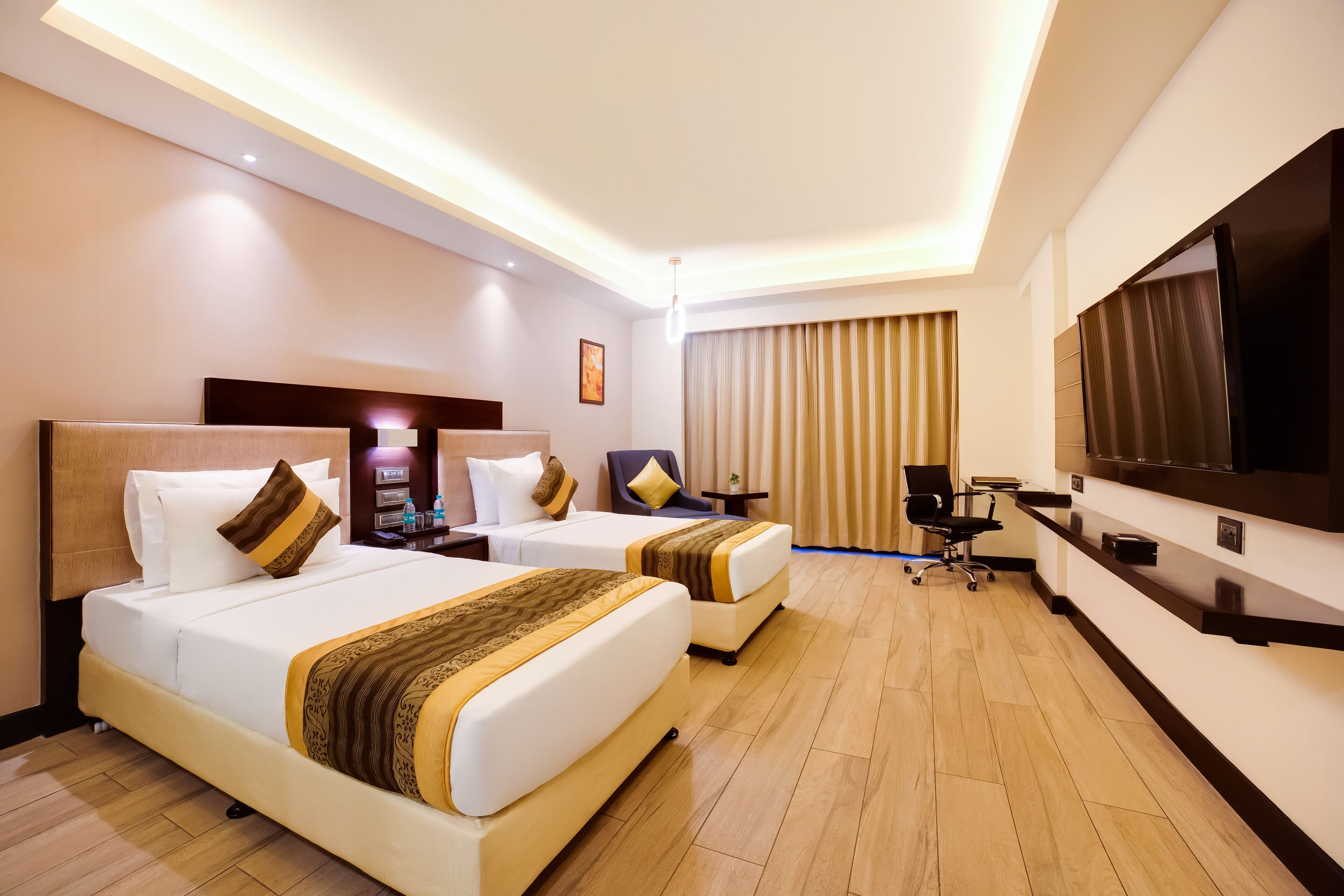 Une chambre d’hôtel avec deux lits, un bureau, une chaise, une télévision et un luminaire au plafond.