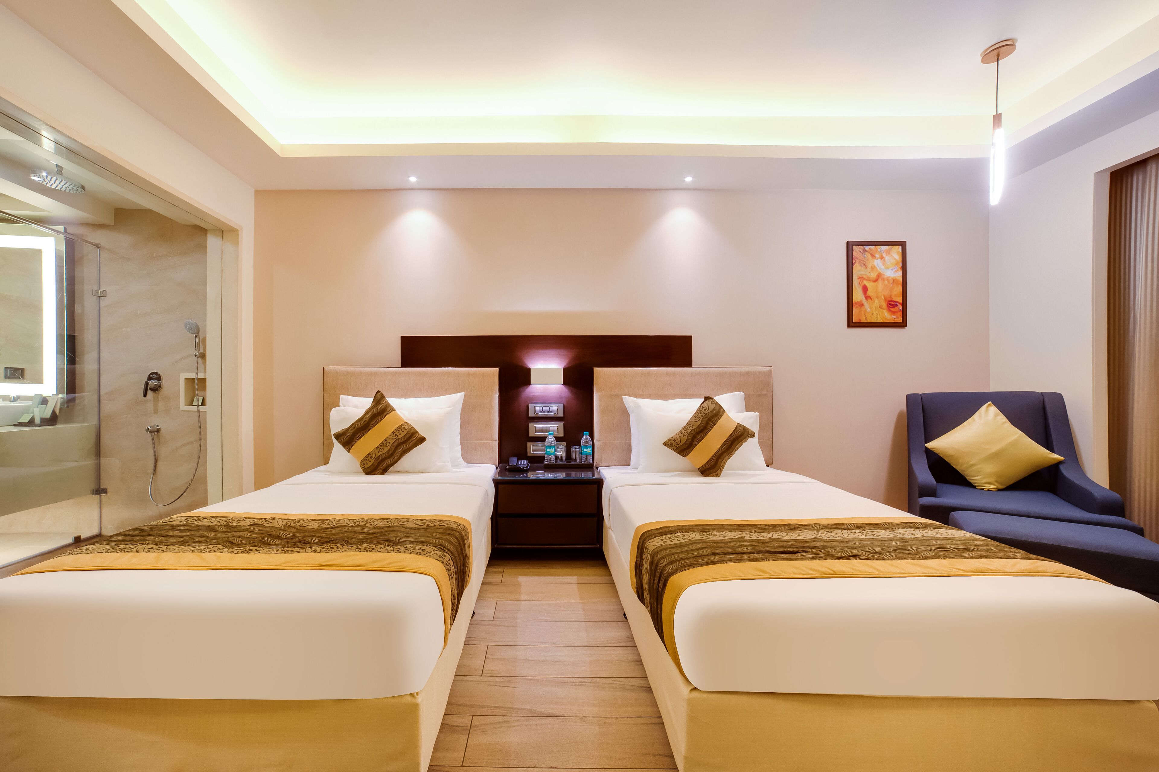 A hotel room with two beds, a nightstand, a chair, and a shower area.