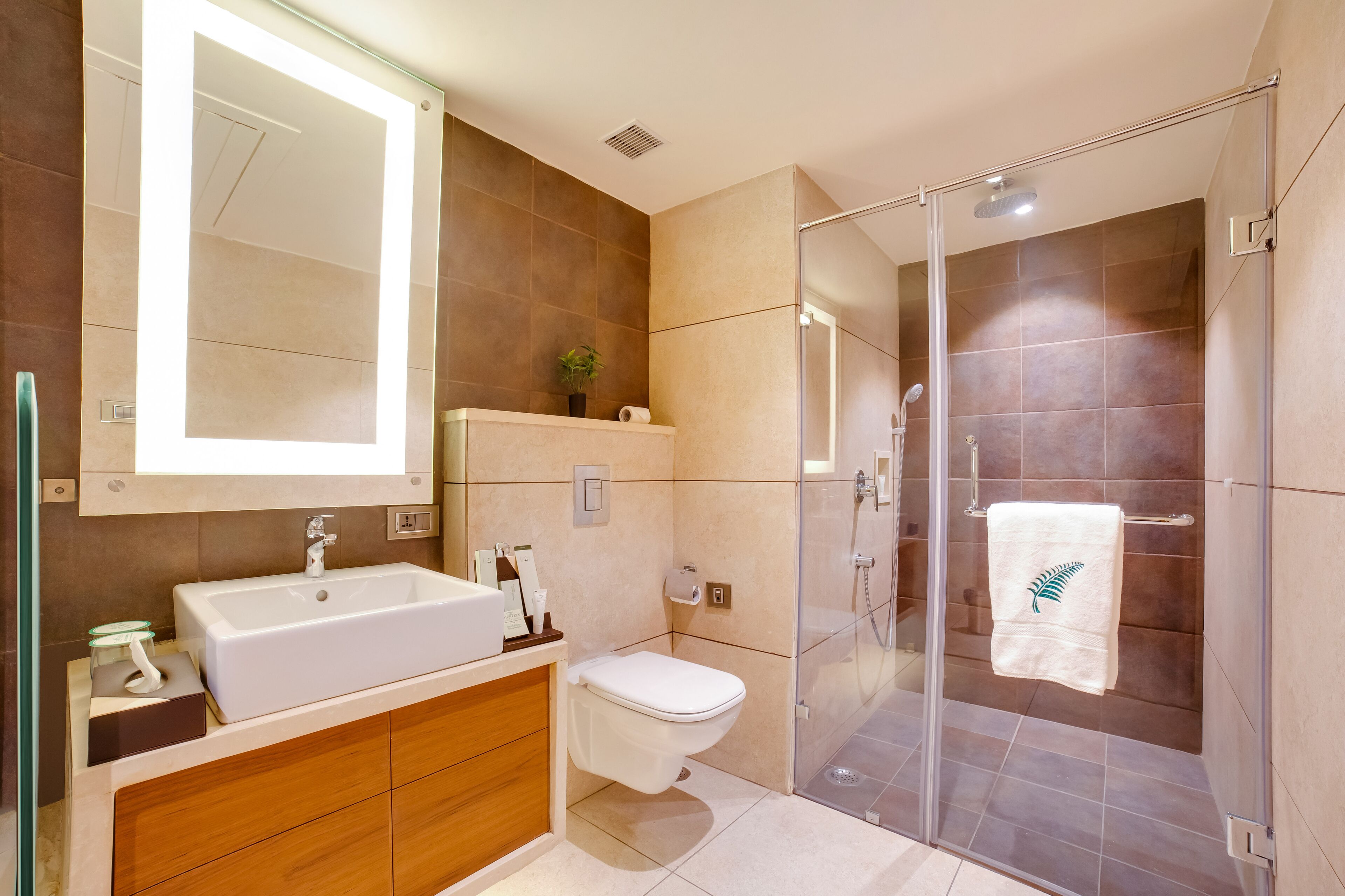 Un baño moderno con un espejo grande, un lavamanos, un inodoro y una zona de ducha con mampara de vidrio.