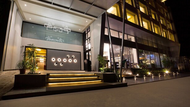 A modern hotel with a well-lit entrance, large windows, and a staircase leading to the lobby.