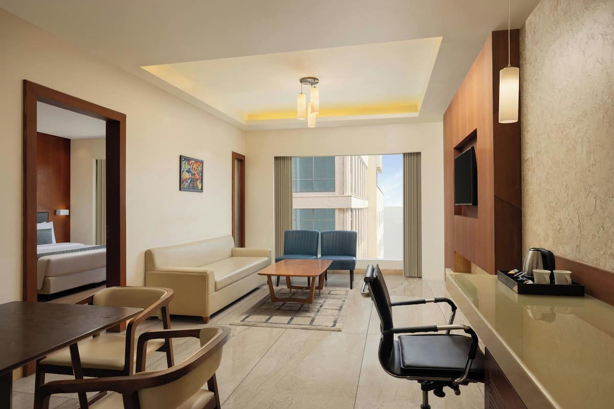 A modern hotel room with a sofa, a dining table, a coffee table, a TV, and a balcony with a view.