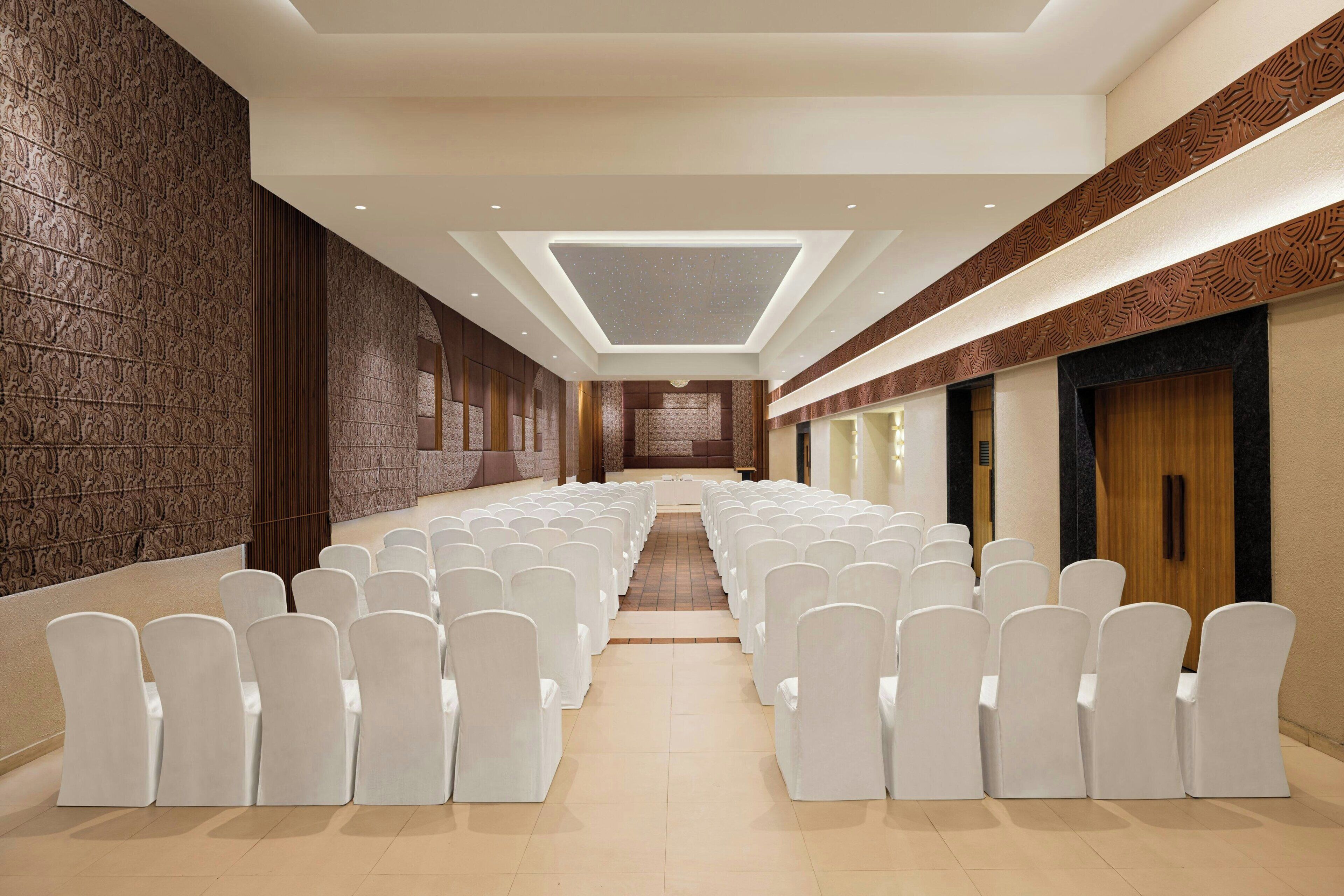 A long, narrow room with rows of white chairs and a central aisle, leading to a stage.