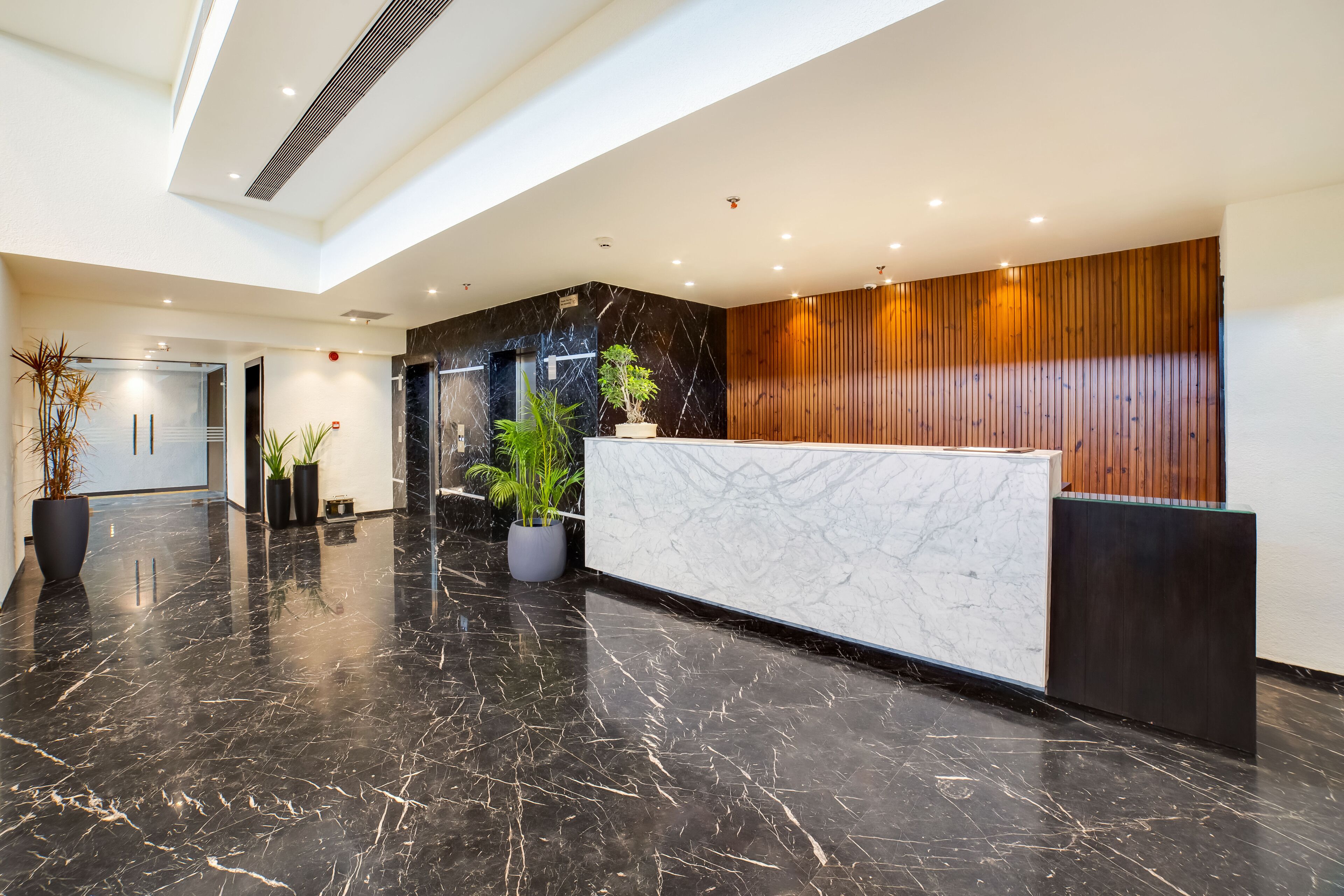 Un área de recepción moderna con un mostrador de mármol, plantas en macetas y un panel de pared de madera.