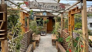 Uma pérgola de madeira com uma placa de 'Welcome', bancos de madeira e plantas em vasos.