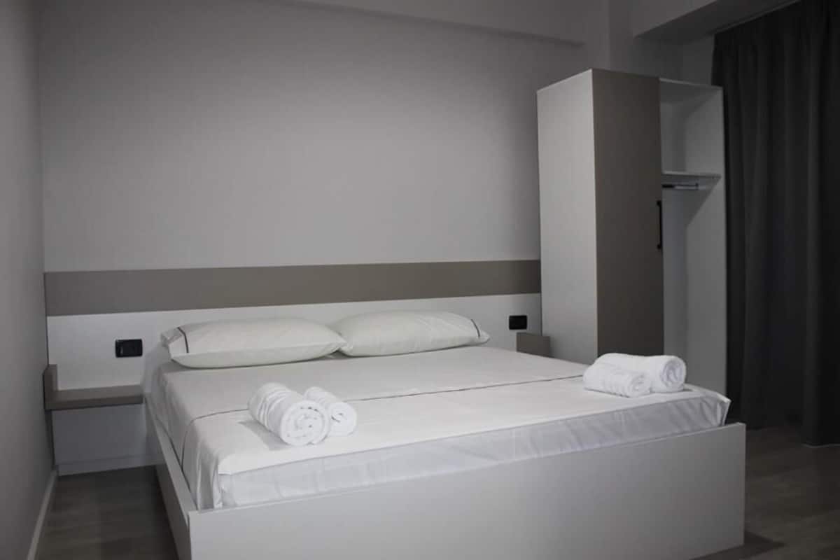 A modern hotel room with a large bed, white linens, and a built-in wardrobe.