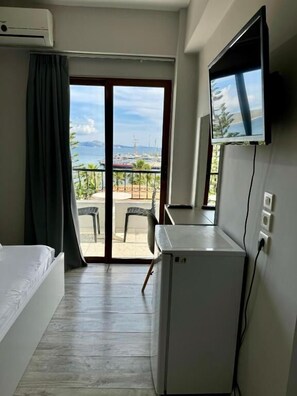 Habitación de hotel con cama, escritorio, televisor y vista al mar y a los barcos a través de una puerta corrediza de vidrio.